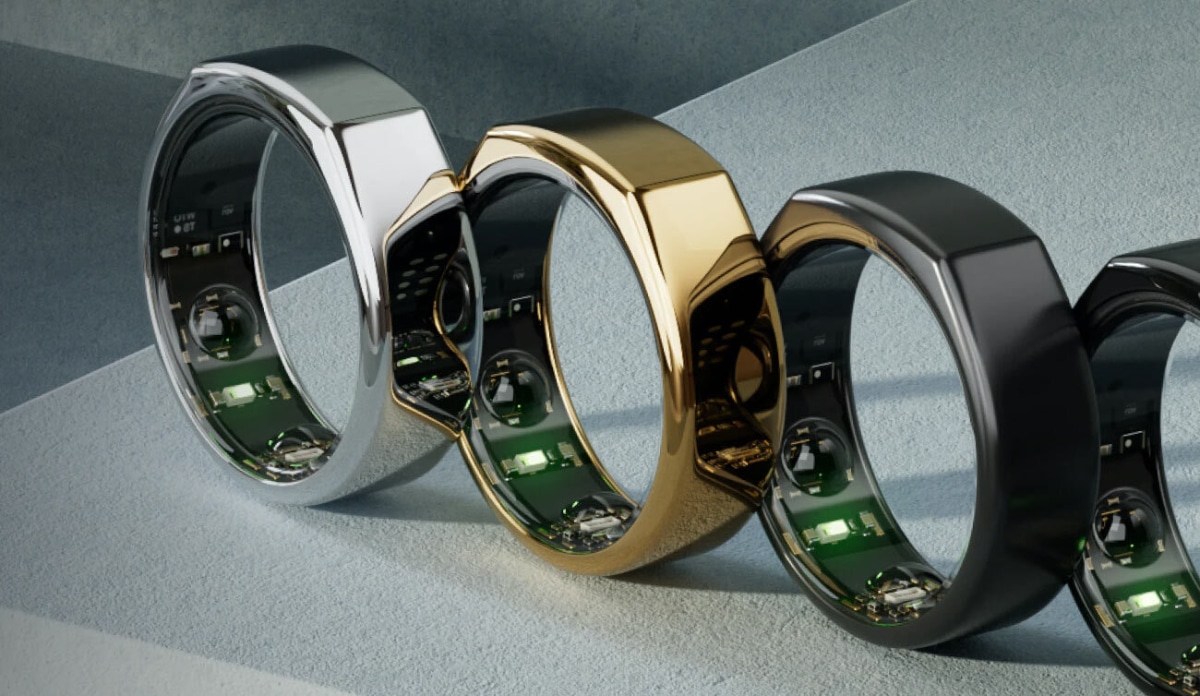 Four sleek, modern rings in silver, gold, and black, showcasing their technological interiors against a textured backdrop.