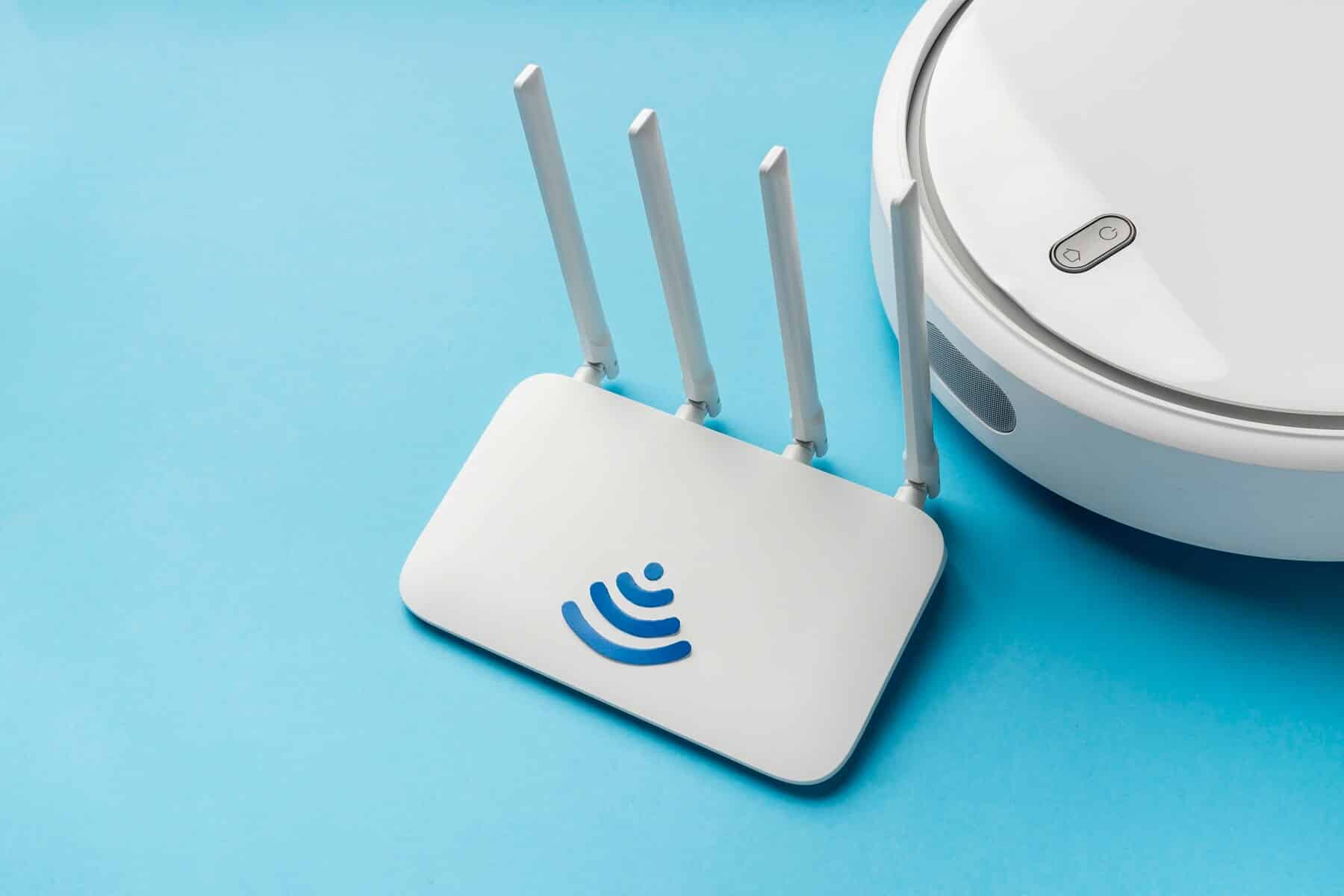 A white Wi-Fi router with four antennas next to a robotic vacuum cleaner on a light blue background.