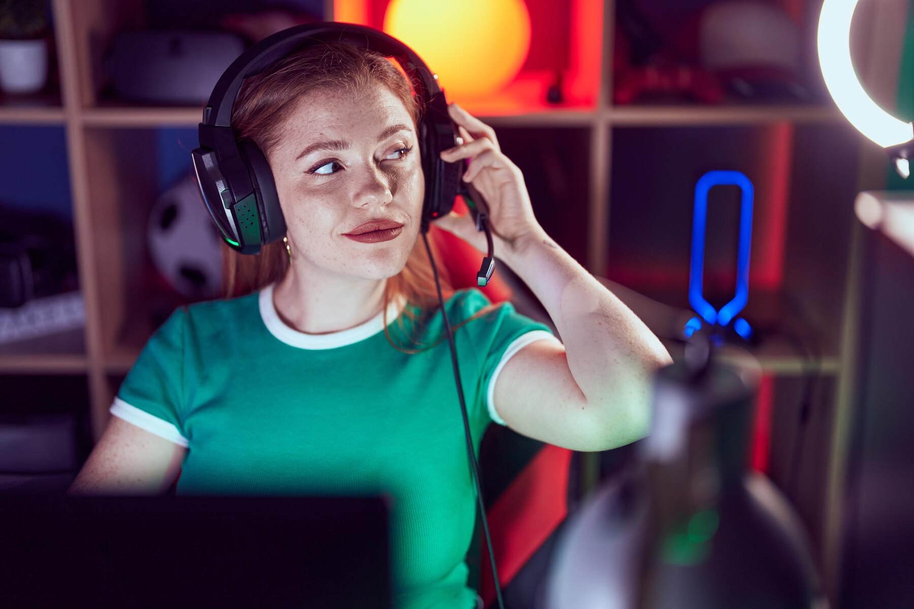 A person wearing a headset sits in front of a laptop, surrounded by colorful lighting and gaming accessories.